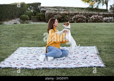 Donna che si diverte con un cane Jack Russell nel parco durante l'autunno. Intimo momento di vita all'aperto con animali domestici, amicizia e colori stagionali. Ideale per famiglie, attività all'aperto e campagne di compagnia di animali domestici. Foto Stock