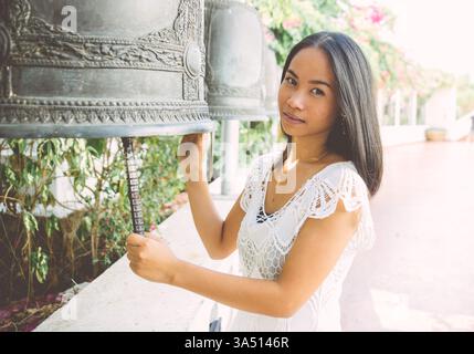 Donna thailandese che visita un tempio buddista, indossa abiti tradizionali e gioielli in una colorata scena culturale. Uno sguardo rispettoso sulla cultura tradizionale e sull'ambientazione del tempio. Foto Stock