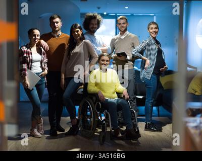 Una donna d'affari disabile in sedia a rotelle lavora con i colleghi in un moderno ufficio open space. Illustra la diversità, l'inclusione e il lavoro di squadra sul luogo di lavoro. Foto Stock