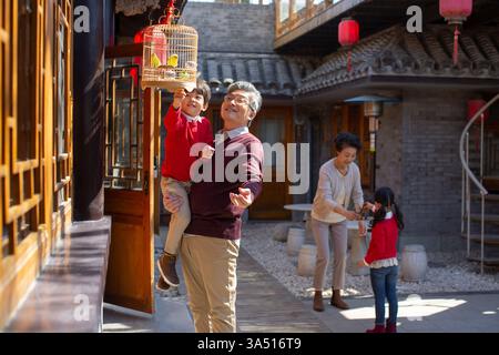 Scena luminosa di nonni cinesi che giocano con i nipoti in un cortile illuminato dal sole. Un momento caldo e multigenerazionale che sostiene storie di famiglia, tradizione e cultura cinese. Ideale per feste in compagnia, feste e vita a casa. Foto Stock