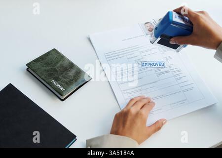 Primo piano di un funzionario consolare che timbra una domanda di visto con un sigillo approvato. La ripresa ad alto angolo enfatizza la documentazione e la procedura ufficiale in un ambiente consolato. Questa immagine funziona bene per l'immigrazione, i visti di viaggio e le comunicazioni relative alle ambasciate. Foto Stock