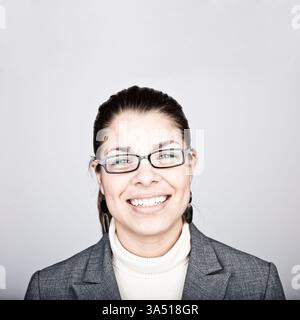Una donna ispanica sorridente che indossa gli occhiali si staglia su uno sfondo grigio. Un ritratto professionale in stile "headshot" che si adatta perfettamente ai materiali aziendali, aziendali e di marketing. Foto Stock