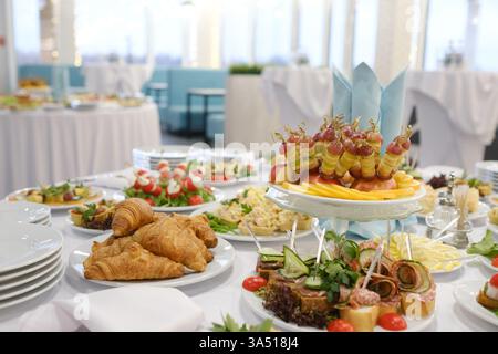 Un vivace buffet in mostra include una varietà di antipasti, frutta fresca e pasticcini disposti su eleganti tavoli in una luminosa e spaziosa area pranzo Foto Stock