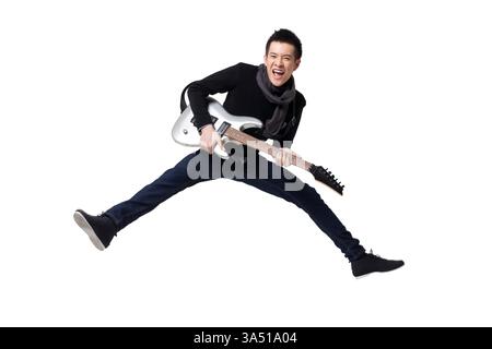 Giovane uomo cinese elegante che suona una chitarra elettrica in uno studio con sfondo bianco. Immagine dinamica e moderna dello stile di vita, adatta alla musica, alla cultura giovanile e al branding della moda. Foto Stock