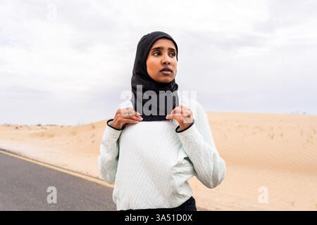 Ritratto di una donna araba del Medio Oriente che indossa un hijab, che si sta allenando all'aperto in un ambiente desertico. Indossa abbigliamento sportivo burkini, sottolineando uno stile di vita attivo nei caldi climi del deserto. Ideale per fitness, allenamenti all'aperto e atleti musulmani in campagne lifestyle o abbigliamento sportivo. Foto Stock