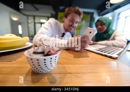 Team di business multiculturale internazionale che collabora, con un uomo e una donna musulmana africana in un hijab verde, che utilizzano un laptop e un telefono cellulare insieme. Questa immagine si adatta al lavoro di squadra aziendale, a luoghi di lavoro diversi e a scenari di ufficio moderni. Ideale per le comunicazioni aziendali e le funzioni di diversità. Foto Stock