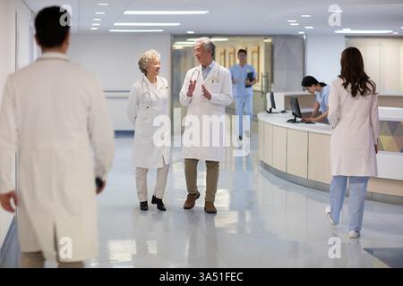 Medici cinesi anziani di sesso maschile e femminile che parlano mentre camminano nel corridoio dell'ospedale Foto Stock