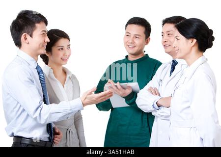 Allegra giovane coppia cinese accanto a un team medico, segnalando assistenza sanitaria di supporto. L'immagine trasmette fiducia, competenza medica e servizio incentrato sul paziente. Adatto per assistenza sanitaria, salute familiare e contenuto medico-paziente. Foto Stock