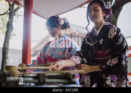 Due donne giapponesi in kimono condividono un gioioso momento di vita all'aperto in una città giapponese. La scena mescola cultura e moda con colori vivaci in un ambiente urbano. Perfetto per i momenti di tradizione, viaggio e multiculturalità. Foto Stock