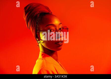 Ritratto di una giovane donna nera elegante con trecce afro in un ambiente da studio. Lo stile alla moda brillante e l'espressione sicura rendono questa immagine versatile per campagne di bellezza e lifestyle. Ideale per il branding, le riviste e la fotografia di prodotti. Foto Stock