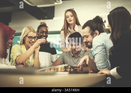 Diversi gruppi di professionisti in un ufficio moderno si prendono una pausa rinfrescante per giocare a scacchi. La scena mette in evidenza il lavoro di squadra, il pensiero strategico e una divertente cultura aziendale. Perfetto per il business, la leadership e i messaggi sulla diversità. Foto Stock