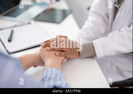 Immagine ravvicinata di una donna che cura la mano di un paziente per confortarlo e rassicurarlo durante una visita medica nella sala esame Foto Stock