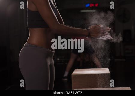 Primo piano di mani con gesso che battono durante un allenamento di arrampicata, con una giovane donna afroamericana. Ideale per il fitness, la palestra interna, l'allenamento di forza e la grafica sportiva. Foto Stock