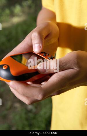 Un uomo adulto all'aperto in un prato con un dispositivo GPS. L'ambiente naturale luminoso mette in evidenza la navigazione e l'esplorazione per viaggi o escursioni a tema. Un'immagine concettuale versatile adatta per campagne di guida, mappatura o avventura all'aperto. Foto Stock