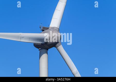 Primo piano della turbina eolica che mostra la torre, la navicella e le enormi pale del rotore contro il cielo blu Foto Stock