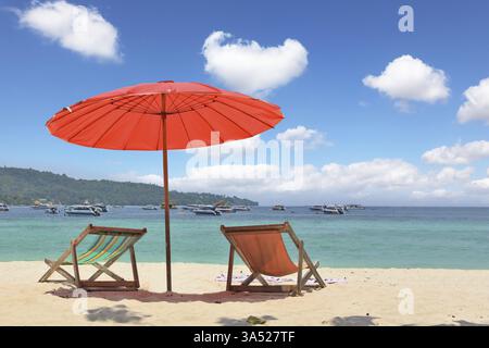 Paradiso tropicale sulle rive del mare azzurro. Ombrellone rosso e sedie a sdraio sulla sabbia bianca Foto Stock