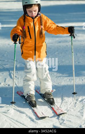 Un giovane sciatore con i capelli intrecciati si muove con grazia su piste innevate, vestito da una giacca arancione brillante pronta ad abbracciare la gioia dell'inverno spor Foto Stock