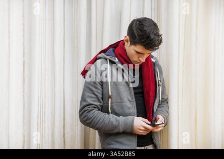 Giovane in piedi al chiuso a digitare un messaggio di testo sul telefono con le dita mentre comunica con gli amici Foto Stock