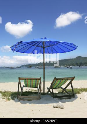 Un pittoresco ombrellone blu scuro e chaise longue a righe su sabbia bianca Foto Stock