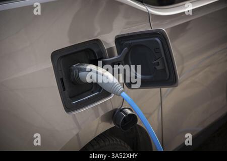 Ricarica di un'auto elettrica presso una stazione di ricarica urbana a bordo strada che mostra un primo piano del connettore e del cavo collegati in un concetto di energia verde Foto Stock