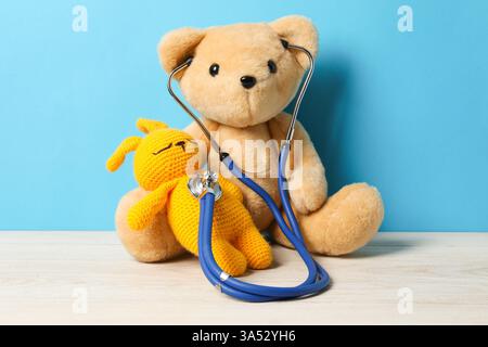 Concetto pediatrico. Orsacchiotto e coniglietto con stetoscopio su tavolo di legno su sfondo azzurro Foto Stock