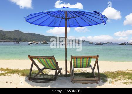 Un pittoresco ombrellone blu scuro e chaise longue a righe su sabbia bianca Foto Stock