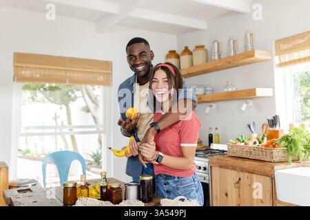 Una coppia felice e variegata in cucina preparando la colazione a base di frutta fresca e godendosi la vacanza insieme Foto Stock
