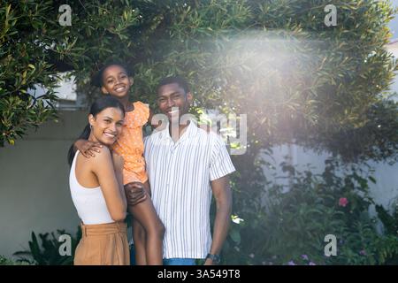 Famiglia sorridente che si gode una vacanza all'aperto, figlia in abito arancione tenuta Foto Stock