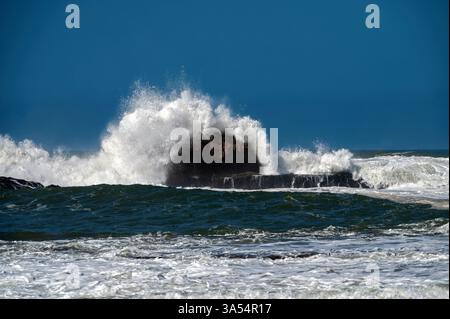 Onde che si infrangono contro la costa rocciosa di Essaouira, in Marocco, durante il cielo azzurro Foto Stock