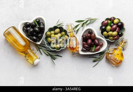 Le ciotole a forma di cuore piene di varie olive, accompagnate da bottiglie di olio d'oliva, creano un vivace spettacolo culinario che celebra il sapore mediterraneo Foto Stock