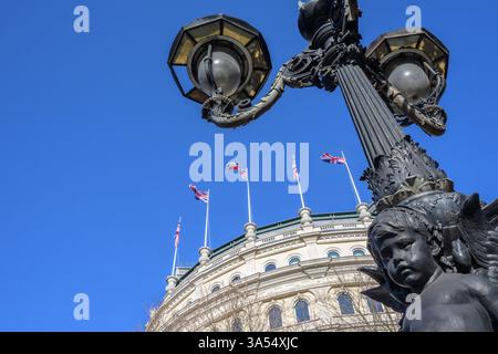Londra, Regno Unito. Palo della lampada in Trafalgar Square (con un "cherubino piangente") e bandiere dell'Unione che sventolano dal tetto del "Grand Building" all'angolo con Foto Stock