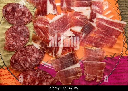 Primo piano di un piatto con fette sottili di prosciutto iberico e salsiccia. Salumi tradizionali spagnoli su una tovaglia colorata. Foto Stock