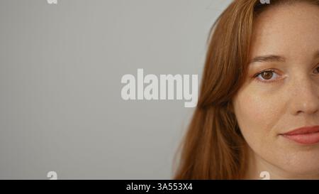 Donna con i capelli rossi che sorride delicatamente su uno sfondo bianco semplice che mostra metà del suo viso in primo piano. Foto Stock