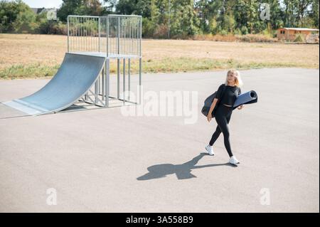 Donna che attraversa la strada e porta con sé un tappetino per yoga Foto Stock
