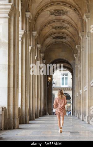 Donna che cammina attraverso un corridoio architettonico a Parigi Foto Stock