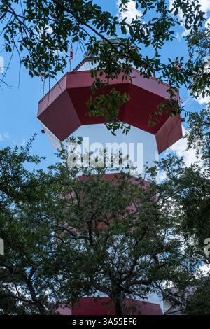 Vista ad angolo basso di un faro rosso e bianco con alberi contro un cielo blu, vista sull'Isola di Hilton Head nell'estate 2022 Foto Stock
