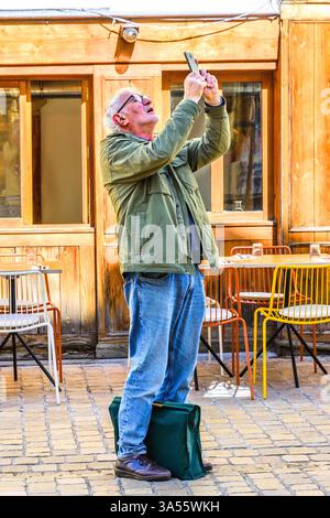 Uomo in strada che tiene in mano lo smartphone e scatta una foto di qualcosa sopra - Tours, Indre-et-Loire (37), Francia. Foto Stock
