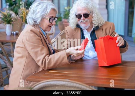 Felice coppia senior caucasica che si scambia un regalo in un caffè all'aperto momento gioioso. Foto Stock
