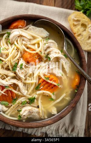 Ciotola di zuppa di spaghetti di pollo con carote su un tovagliolo e fette di baguette su un tavolo di legno. Vista dall'alto Foto Stock