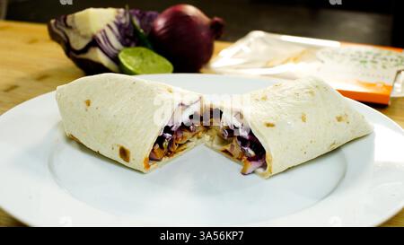 Un taco, chimichanga, enchilada o fajita servito e tagliato a metà su un piatto bianco. Foto Stock