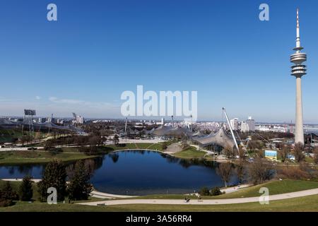 Monaco, Germania. 20 marzo 2025. Il sito olimpico nel Parco Olimpico con la Torre Olimpica di Monaco (Baviera) si riflette nel Lago Olimpico. Il Parco Olimpico di Monaco è un parco cittadino nel quartiere di Oberwiesenfeld ed è stato sede dei Giochi Olimpici del 1972. Il parco olimpico è gestito dall'Olympiapark München GmbH. Crediti: Matthias Balk/dpa/Alamy Live News Foto Stock