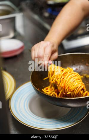 Lo chef prepara con cura una porzione di spaghetti ricoperti da una ricca salsa di pomodoro. La pasta fumante viene piegata elegantemente nella padella prima di essere collocata a. Foto Stock