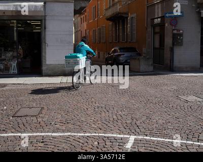 Cremona, Italia 15 marzo 2025 consegna uomo in bicicletta con merce in cassa su strada acciottolata Foto Stock