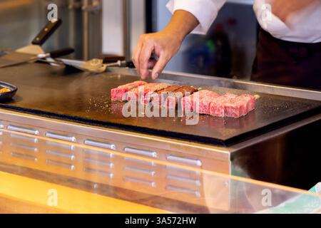 Lo chef griglierà spiedini di manzo wagyu marmorizzato su una superficie teppanyaki calda in un mercato di Tokyo cucendo alla perfezione la carne tenera con una ricca consistenza A. Foto Stock