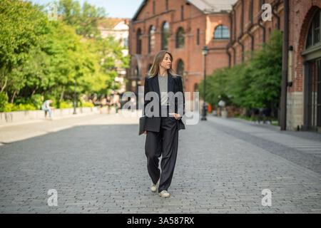 Elegante imprenditrice donna con laptop passeggia per le strade urbane, nomade digitale e freelance Foto Stock