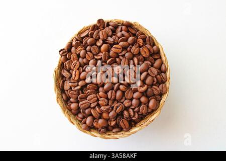 Chicchi di caffè tostati in un cestello intrecciato su uno sfondo bianco pulito. Configurazione minimalista e luminosa, perfetta per annunci di caffè, confezioni e temi alimentari. Foto Stock