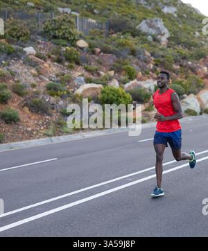 Uomo che corre su strada in natura, indossa canotta rossa e pantaloncini blu, copia spazio Foto Stock