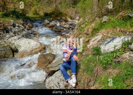 Una ragazza siede vicino a un fiume di montagna su rocce in una giornata di sole. Hinter-tux foto di alta qualità Foto Stock