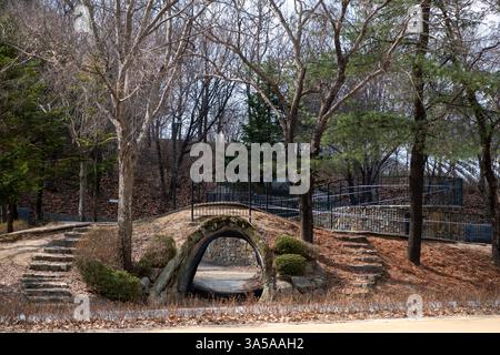 Una collina a tunnel, simile a una grotta. Circondato da alberi, cespugli e gradini in pietra che conducono ad un sentiero recintato. Nella foresta di Seoul Foto Stock