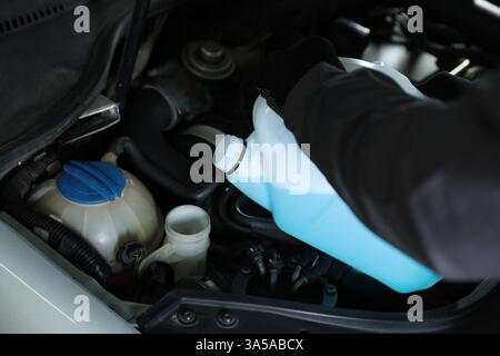 Uomo che versa il lavavetri dal contenitore in plastica nel serbatoio dell'auto, primo piano Foto Stock